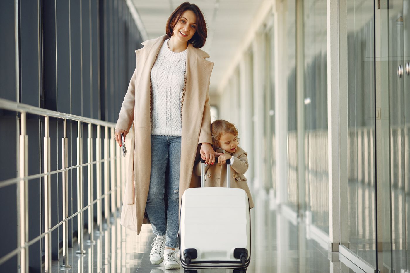 A mother and child with a suitcase walking through an airport jet bridge